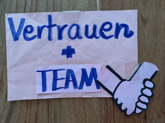 Handgeschriebener Praxisimpuls „Vertrauen + TEAM“ mit Handschlag.